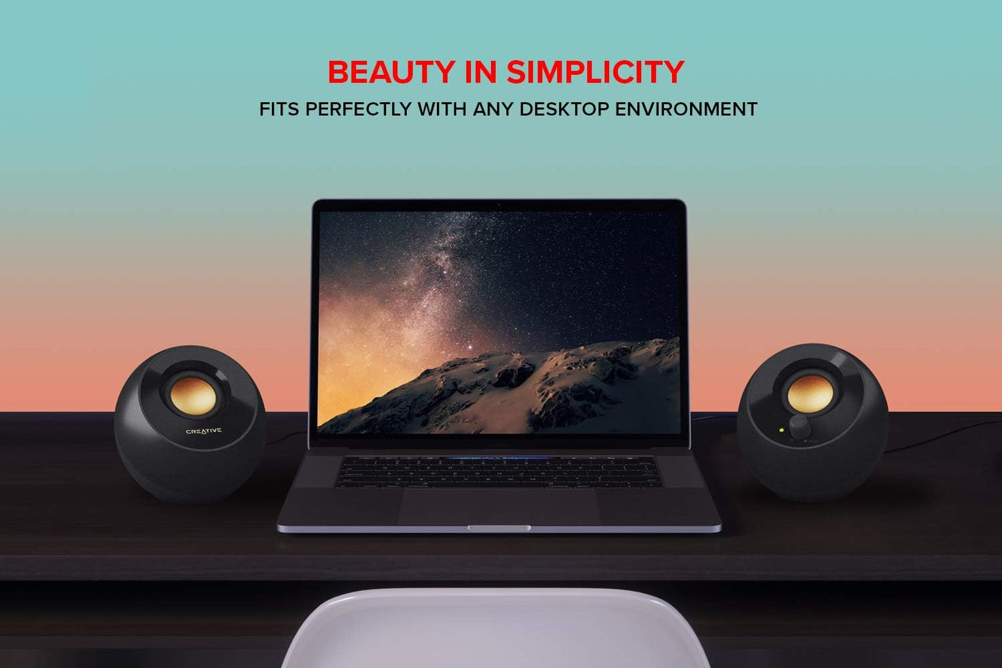 Laptop on a desk with two creative speakers on either side, against a gradient background with 'Beauty in Simplicity' text.