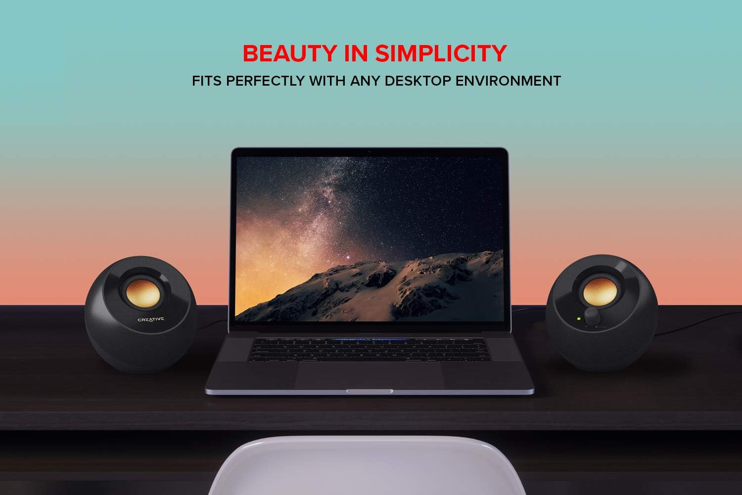 Laptop on a desk with two creative speakers on either side, against a gradient background with 'Beauty in Simplicity' text.