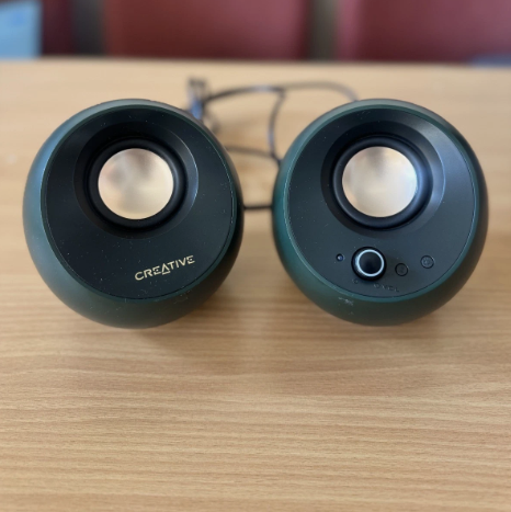A pair of Creative dome-shaped computer speakers in a dark green color, placed on a light wood tabletop with their connecting cable visible behind them.